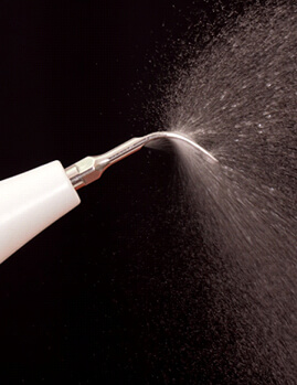 Close-up of ultrasonic scaler spraying water against dark background