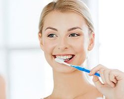 woman brushing teeth to care for dental implants in Dallas, GA