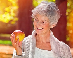 woman with dental implants in Dallas, GA smiles at apple