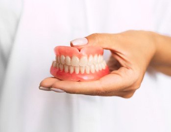 person in white lab coat holding full denture