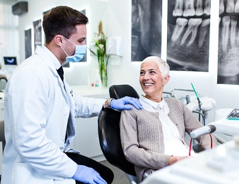 An older woman seated in the dentist’s chair listening to her dentist discuss gum recontouring