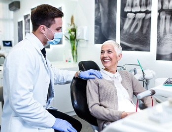 An older woman seated in the dentist’s chair listening to her dentist discuss gum recontouring
