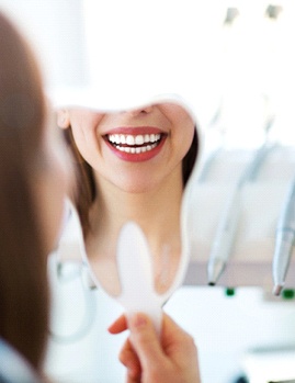 A woman admiring her smile in the mirror at the dentist’s office in Dallas