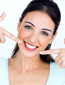 A young female pointing to her smile after teeth whitening in Dallas