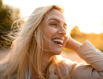 Woman with veneers in Dallas, TX brushing hair out of face