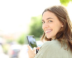 Woman with veneers in Dallas, GA smiling while looking at phone