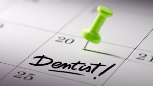 Green push pin stuck into a date on a calendar above the word "Dentist"