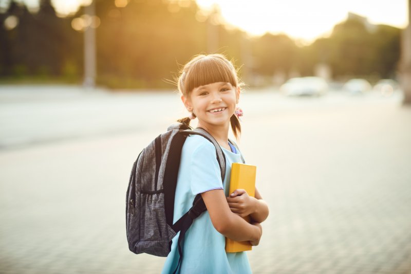 young girl with backpack and books smiling