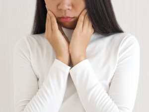 a woman holding the sides of her mouth due to untreated TMJ disorder