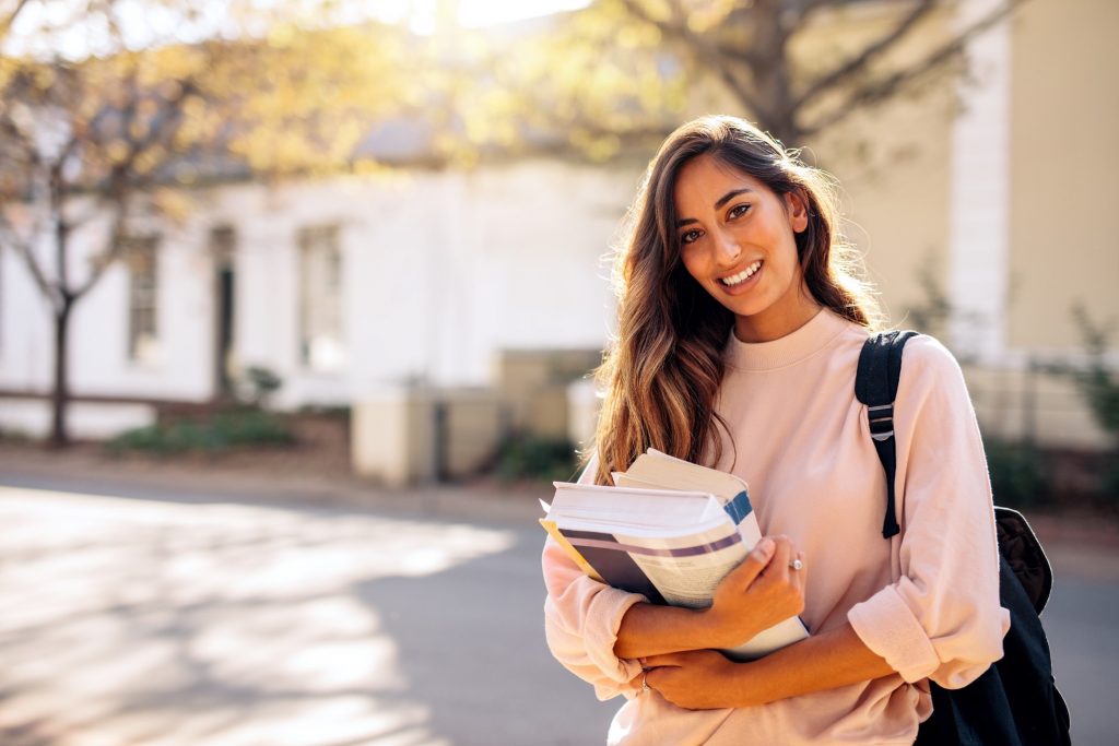 College student smiling while holding books on campus