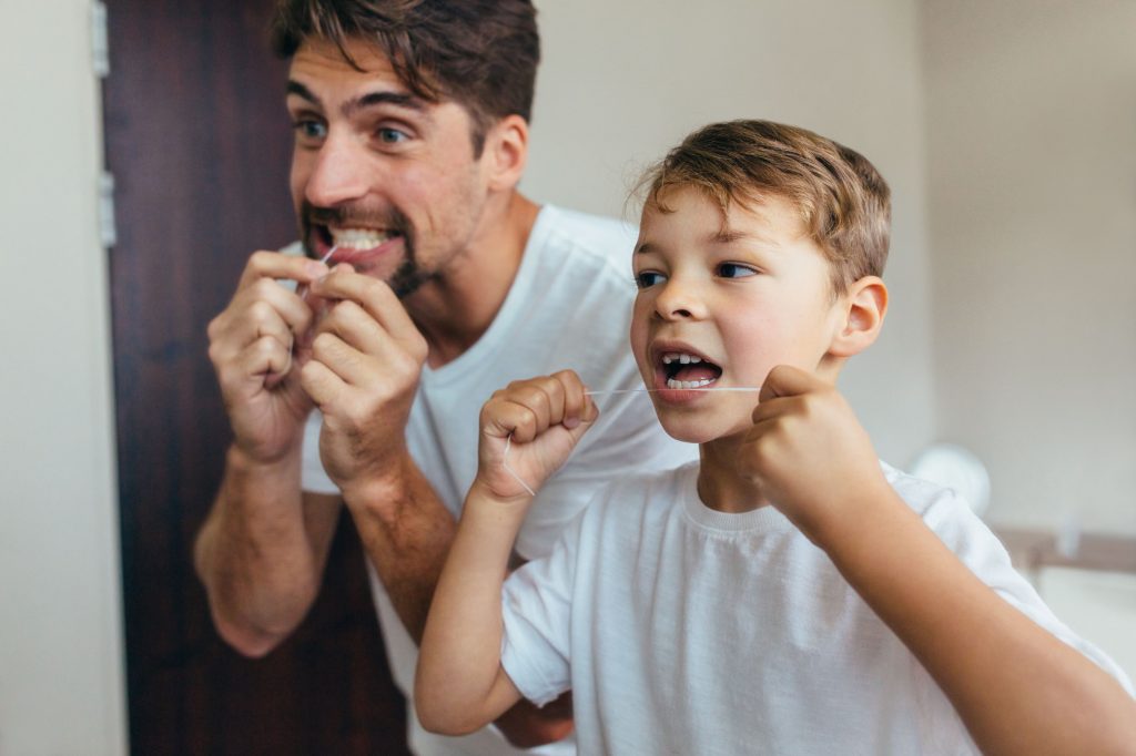 Man and boy in white shirt flossing teeth. 