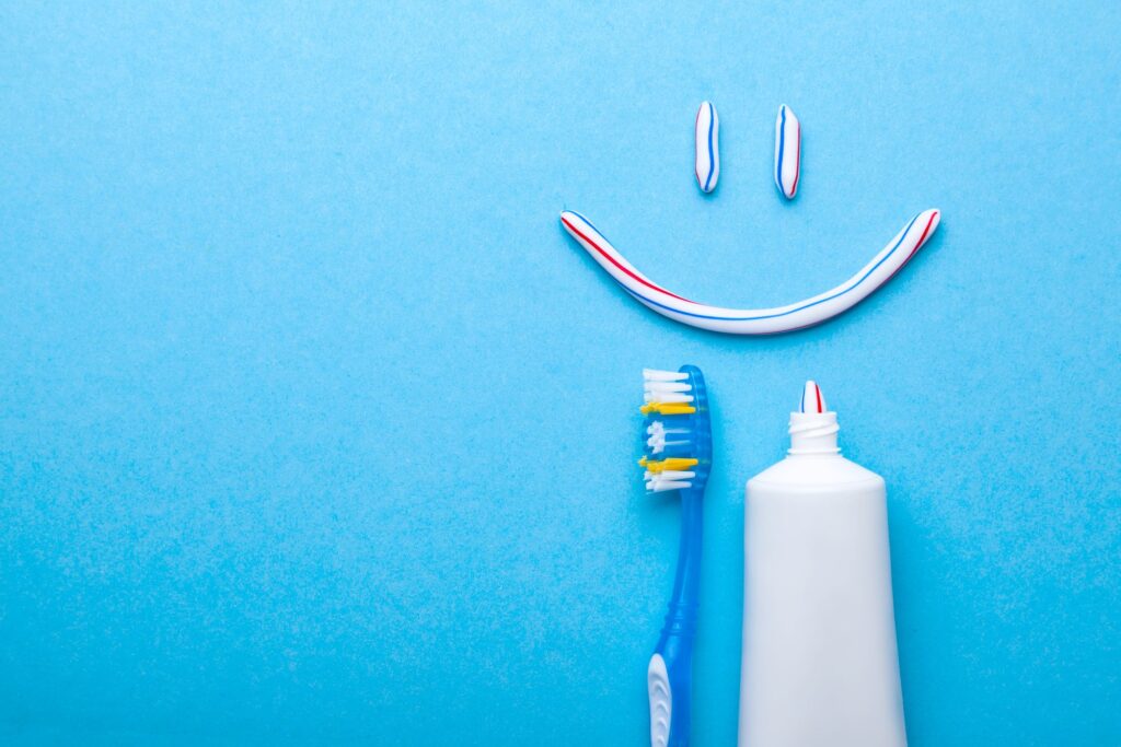 Smiley made out of toothpaste next to toothbrush on light blue surface
