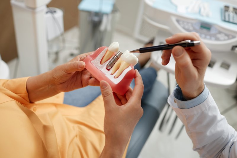 An obscured senior woman holding an enlarged dental implant model
